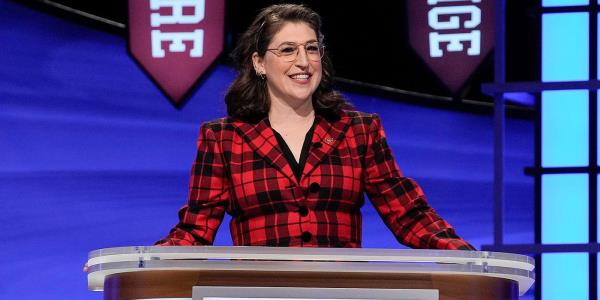 Mayim Bialik standing behind a podium as Jeopardy host